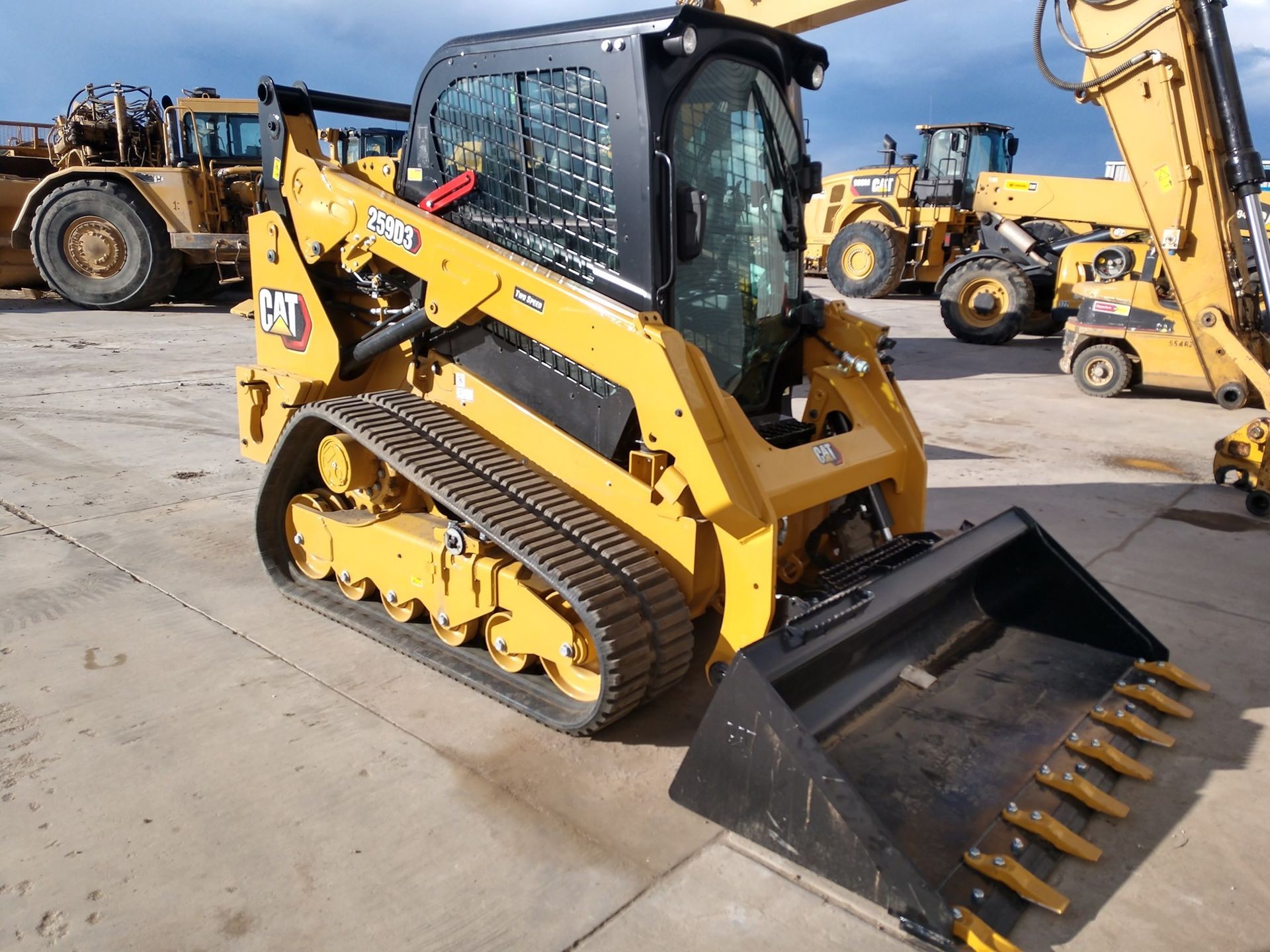 Yellow skid steer loader parked on a concrete lot with other construction vehicles in the background.