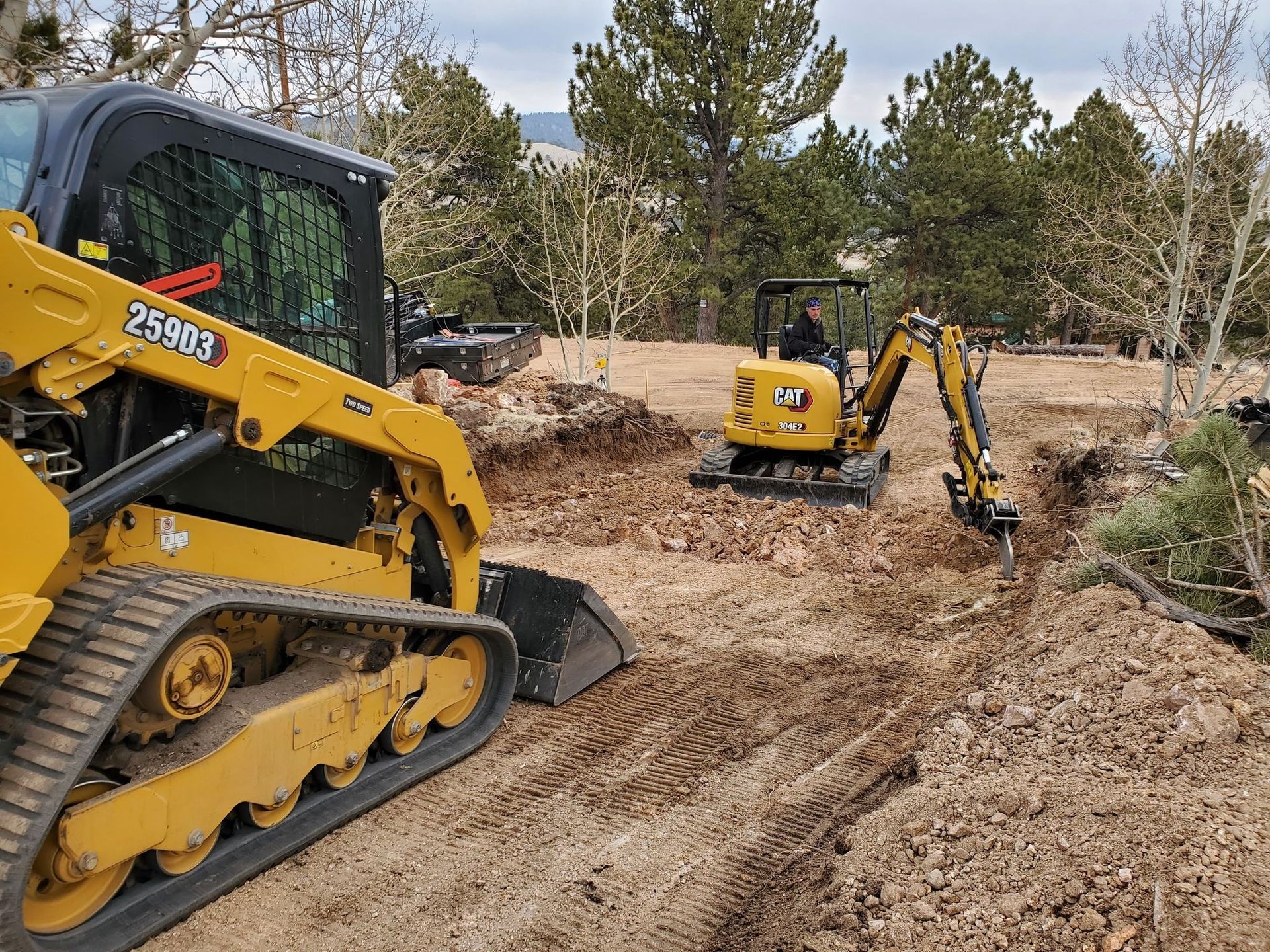 Construction site with yellow bulldozer and mini excavator digging earth, surrounded by trees.